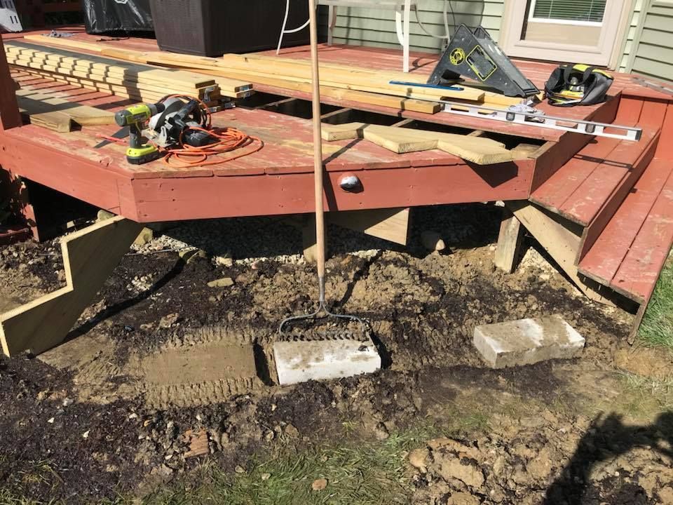A rake is sitting on top of a pile of dirt next to a wooden deck.