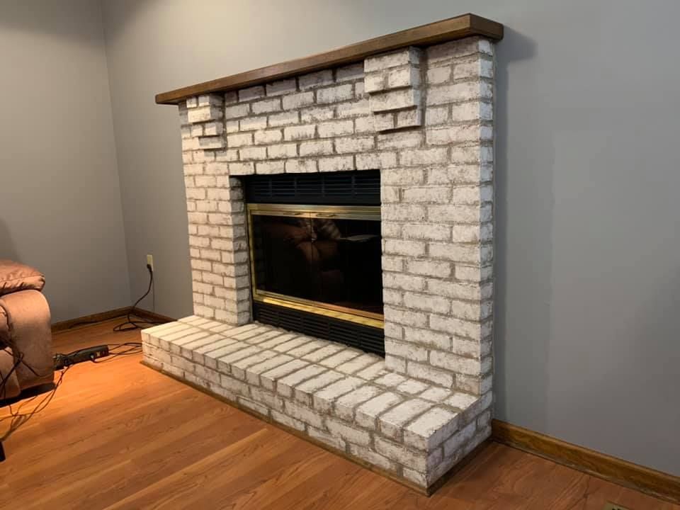 A white brick fireplace in a living room with a wooden floor.