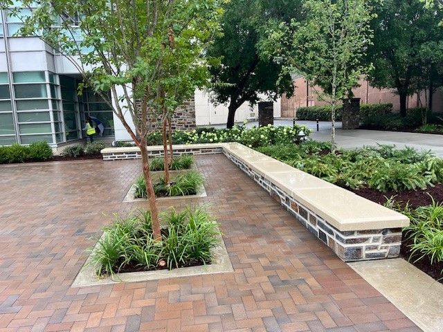 Brick courtyard with trees, stone planter boxes, and a long stone bench.