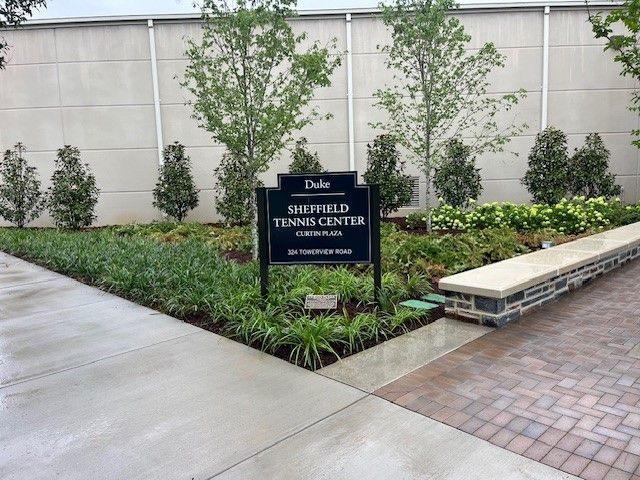 Sign for Sheffield Tennis Center at Duke University. Black sign, landscaping.