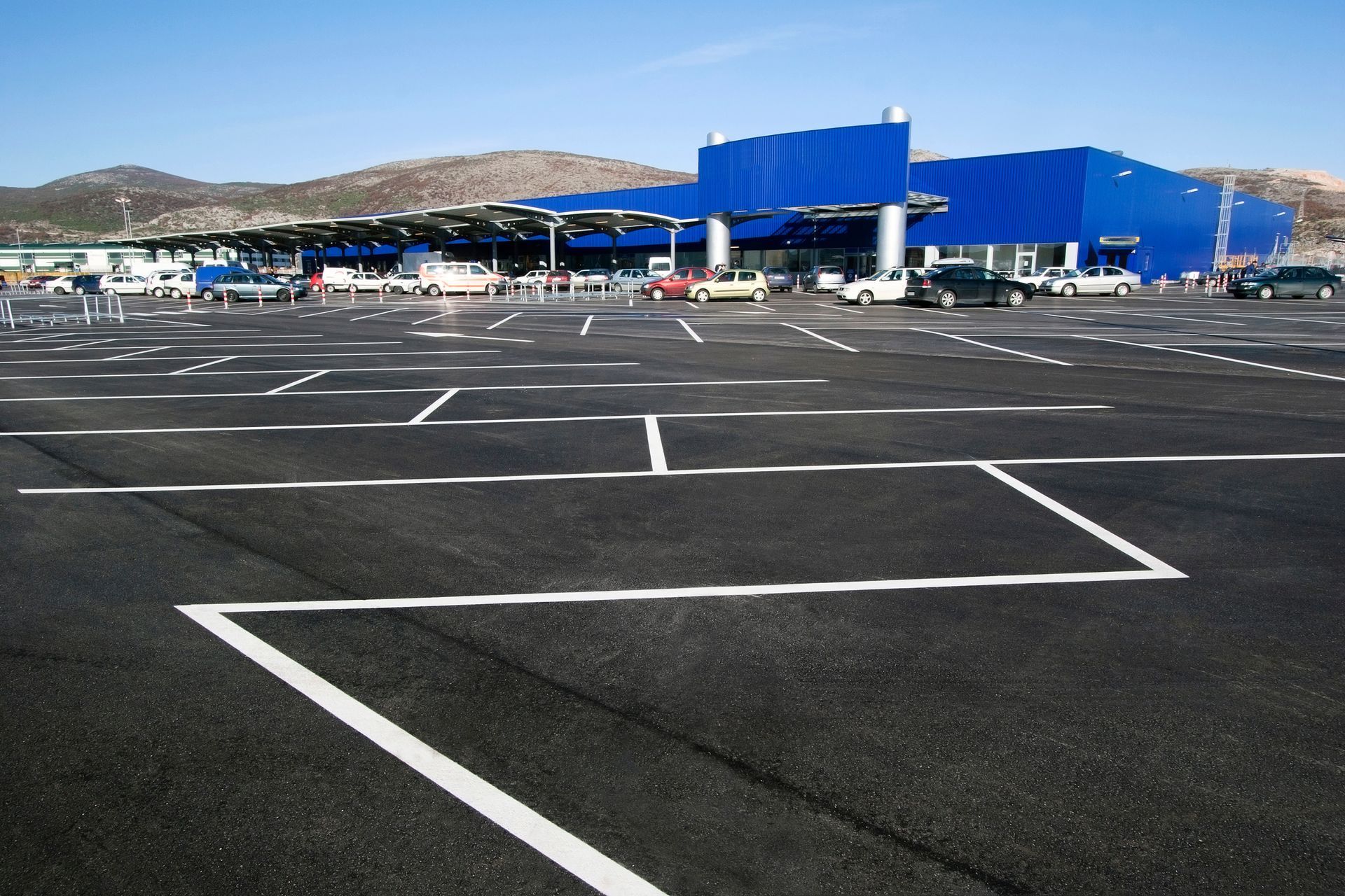 Empty parking lot with white markings in front of a blue building and distant hills Empty parking lot with white markings in front of a blue building and distant hills