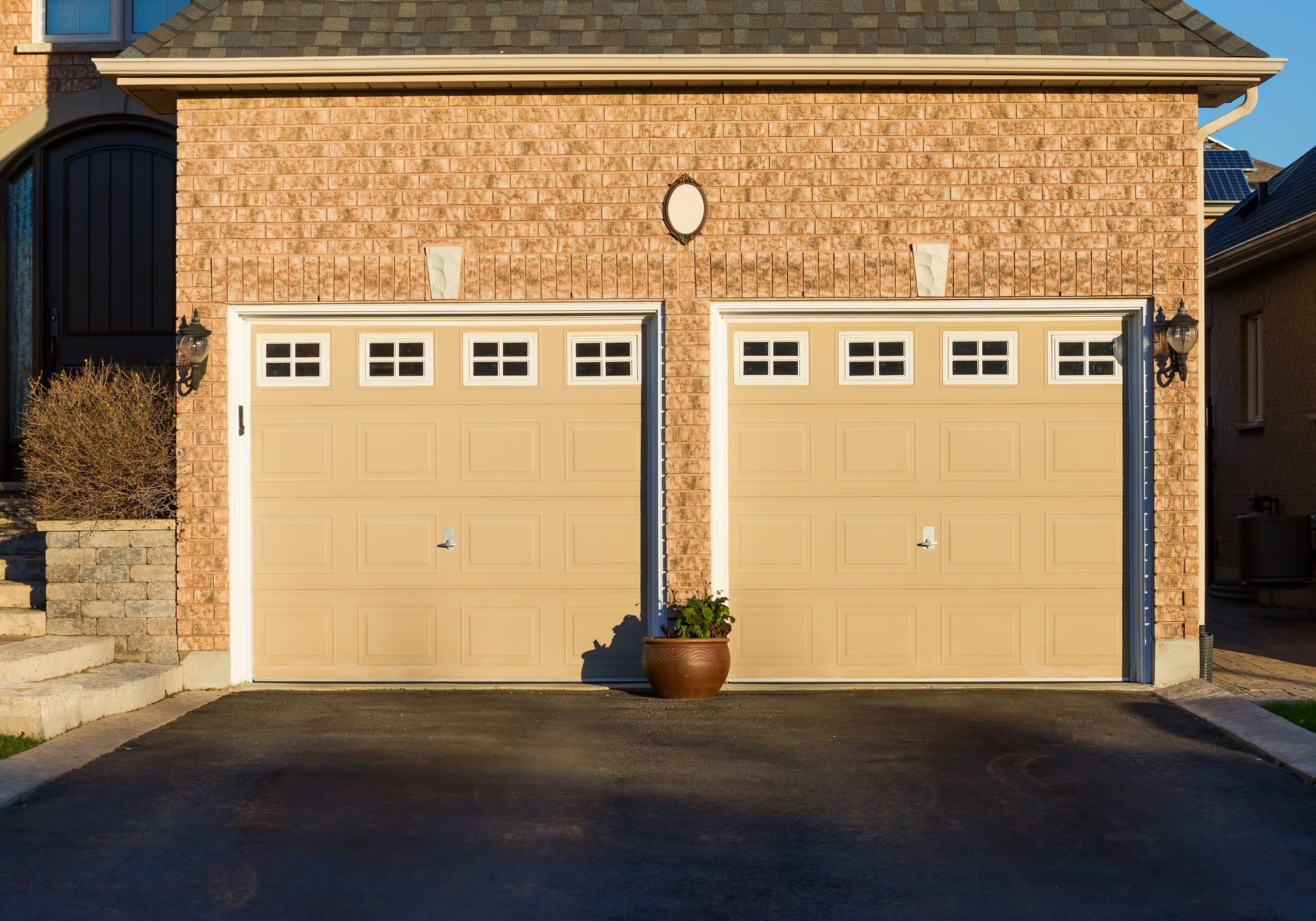 Two beige garage doors on a brick house with a potted plant centered between them Two beige garage doors on a brick house with a potted plant centered between them