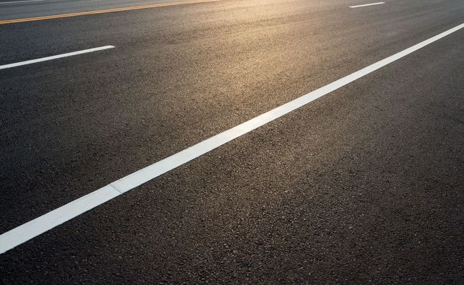 Empty asphalt road with white lane markings Empty asphalt road with white lane markings