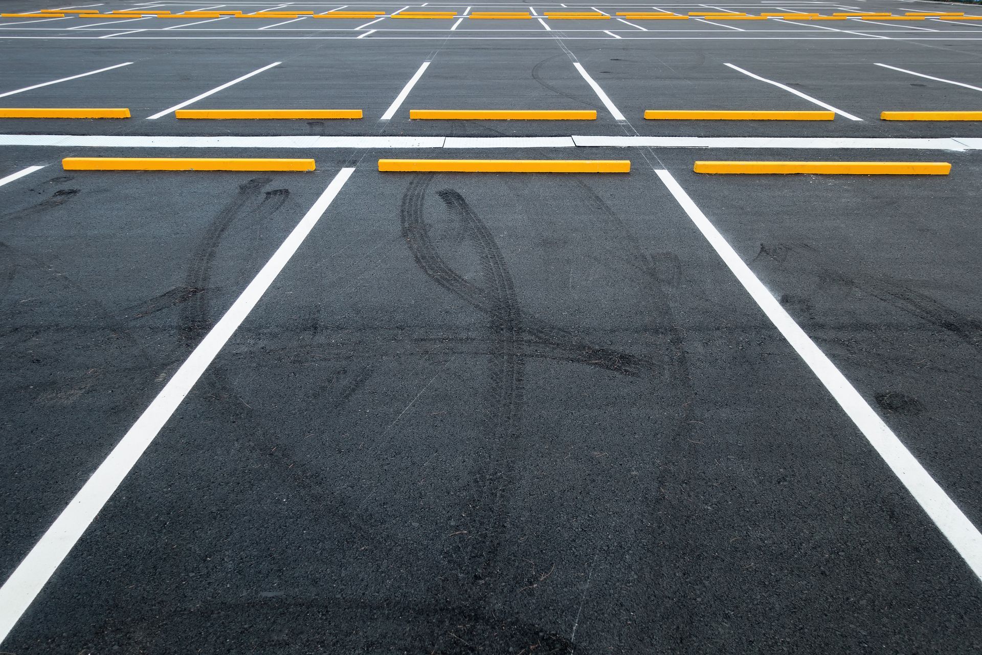 Empty parking lot with white lines and yellow wheel stops on dark asphalt Empty parking lot with white lines and yellow wheel stops on dark asphalt