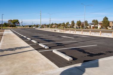 Empty parking lot with fresh black pavement and white parking stops under a clear sky Empty parking lot with fresh black pavement and white parking stops under a clear sky