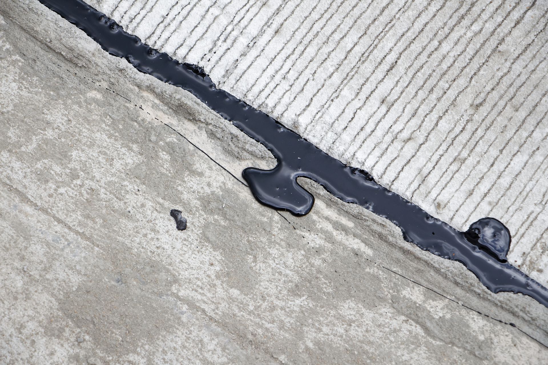 Cracked concrete and corrugated metal roof seam sealed with black caulk Cracked concrete and corrugated metal roof seam sealed with black caulk