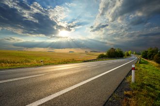 Country road at sunset under dramatic clouds, with golden fields and a reflective wet pavement Country road at sunset under dramatic clouds, with golden fields and a reflective wet pavement