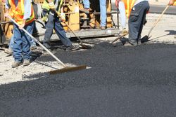Road crew paving asphalt with rakes around a construction vehicle Road crew paving asphalt with rakes around a construction vehicle