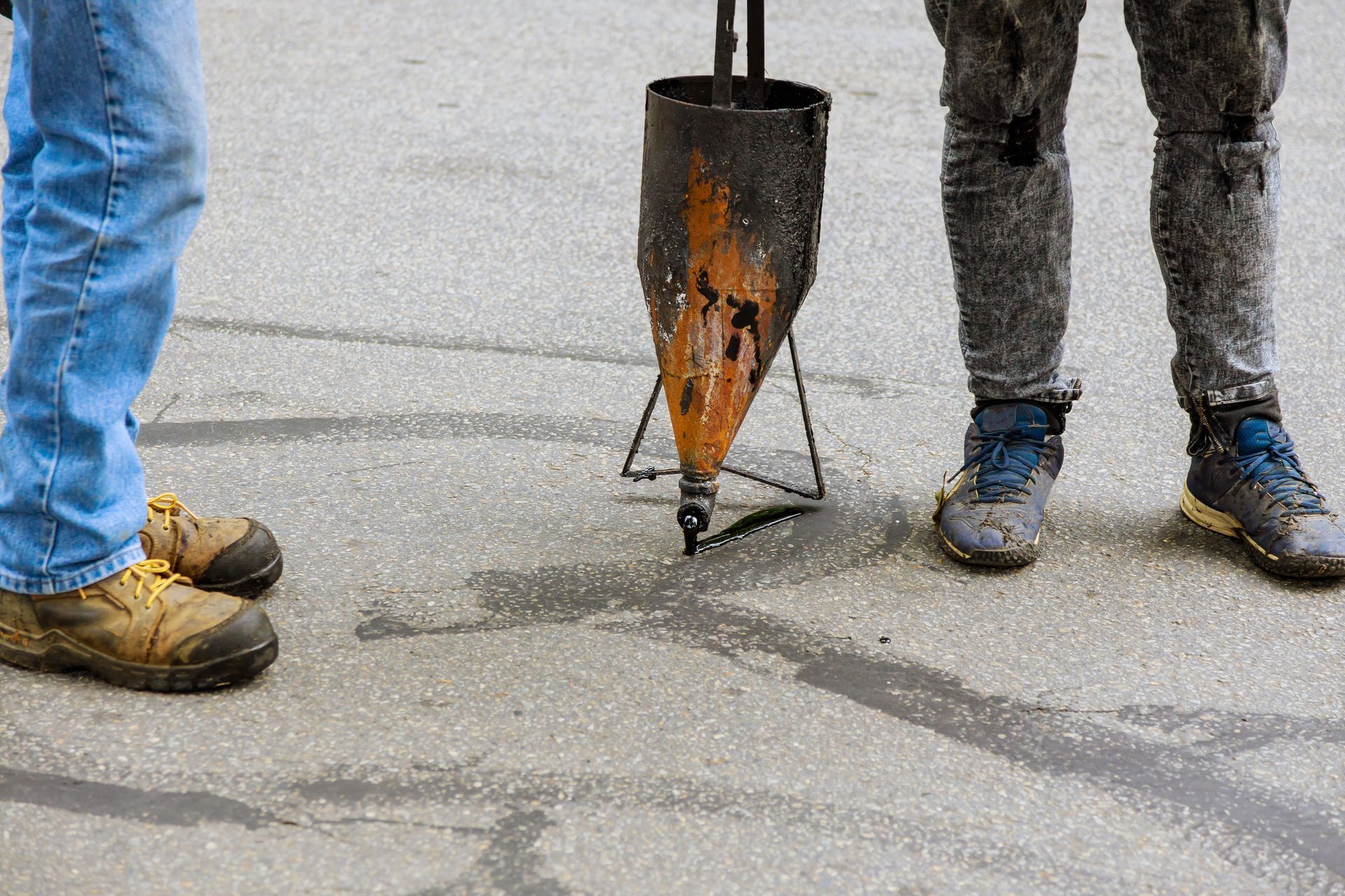 Workers standing around a pavement crack repair tool on wet asphalt, with shovels and boots visible Workers standing around a pavement crack repair tool on wet asphalt, with shovels and boots visible