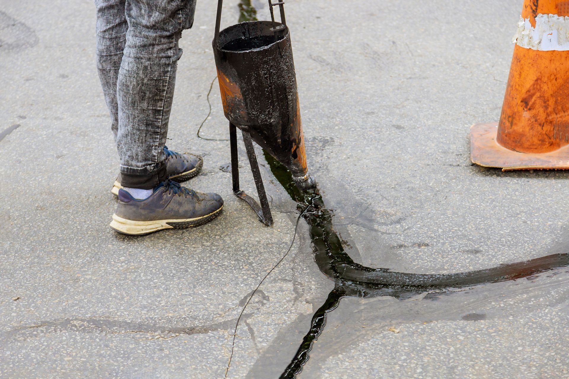 Worker standing by a cracked sidewalk beside a black utility barrel and orange traffic cone Worker standing by a cracked sidewalk beside a black utility barrel and orange traffic cone