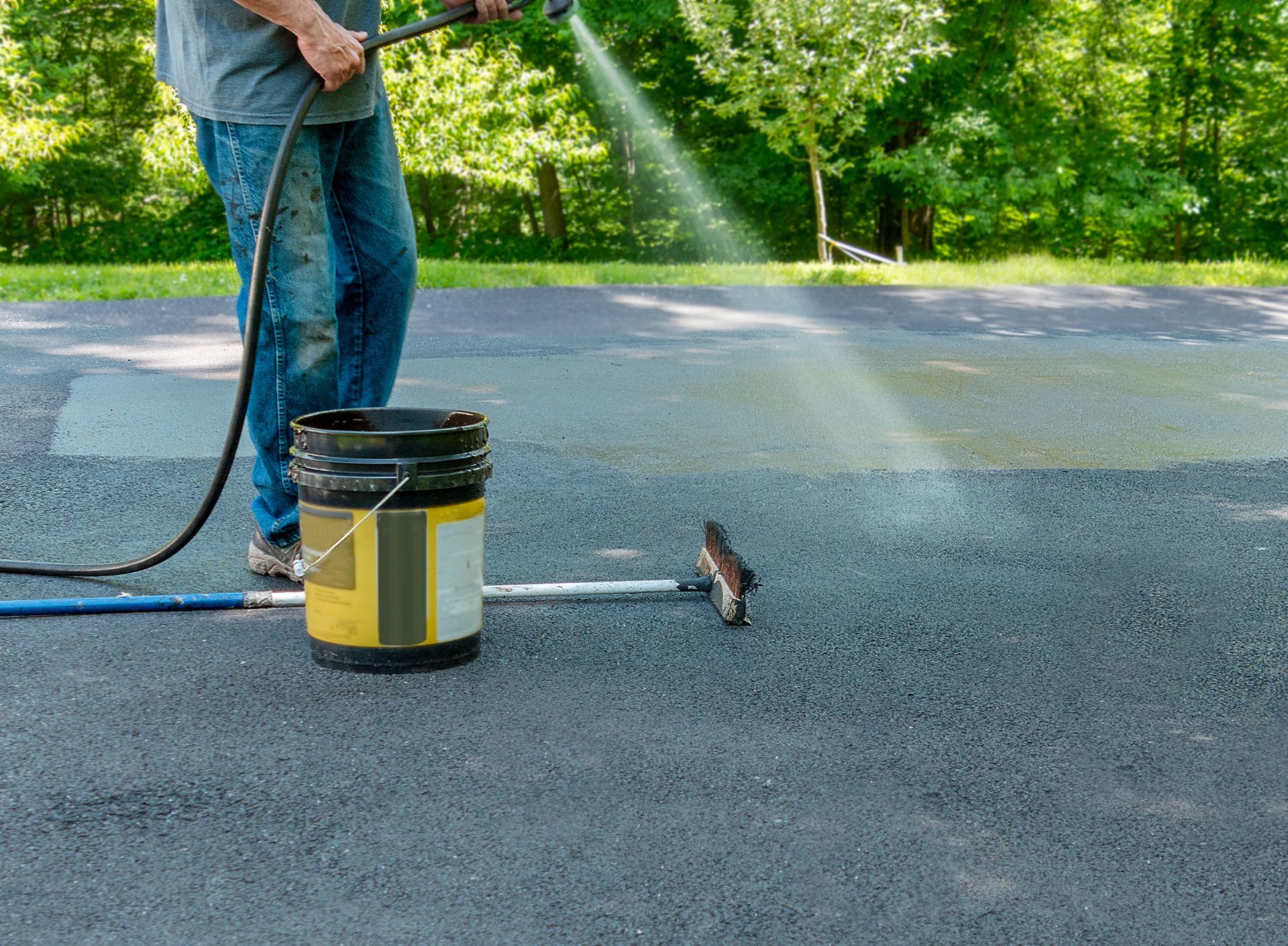 Person pressure-washing a driveway with a hose and sprayer near a paint can-like bucket Person pressure-washing a driveway with a hose and sprayer near a paint can-like bucket