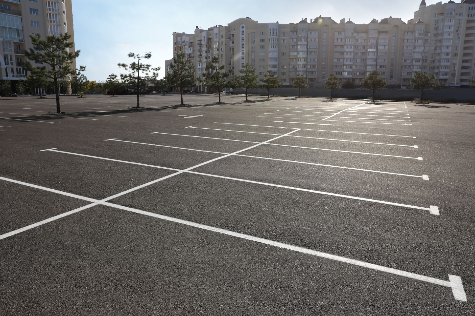 Empty sunlit parking lot with white markings in front of apartment buildings Empty sunlit parking lot with white markings in front of apartment buildings