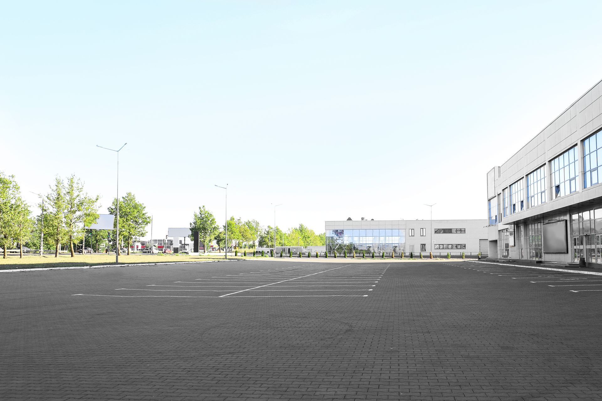 Empty paved courtyard beside a modern building, with trees and a bright sky in the background Empty paved courtyard beside a modern building, with trees and a bright sky in the background