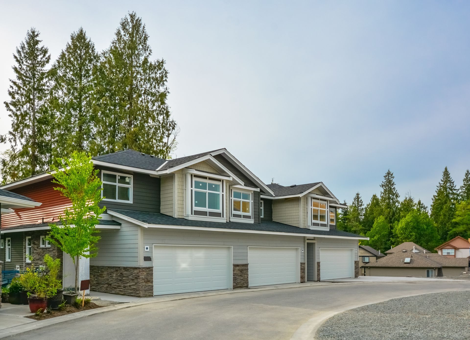 Modern gray townhouse with white garage doors and tall evergreen trees in the background Modern gray townhouse with white garage doors and tall evergreen trees in the background