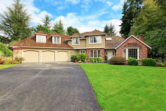 Suburban house with beige and brick exterior, two-car garage, green lawn, and driveway under a blue sky Suburban house with beige and brick exterior, two-car garage, green lawn, and driveway under a blue sky