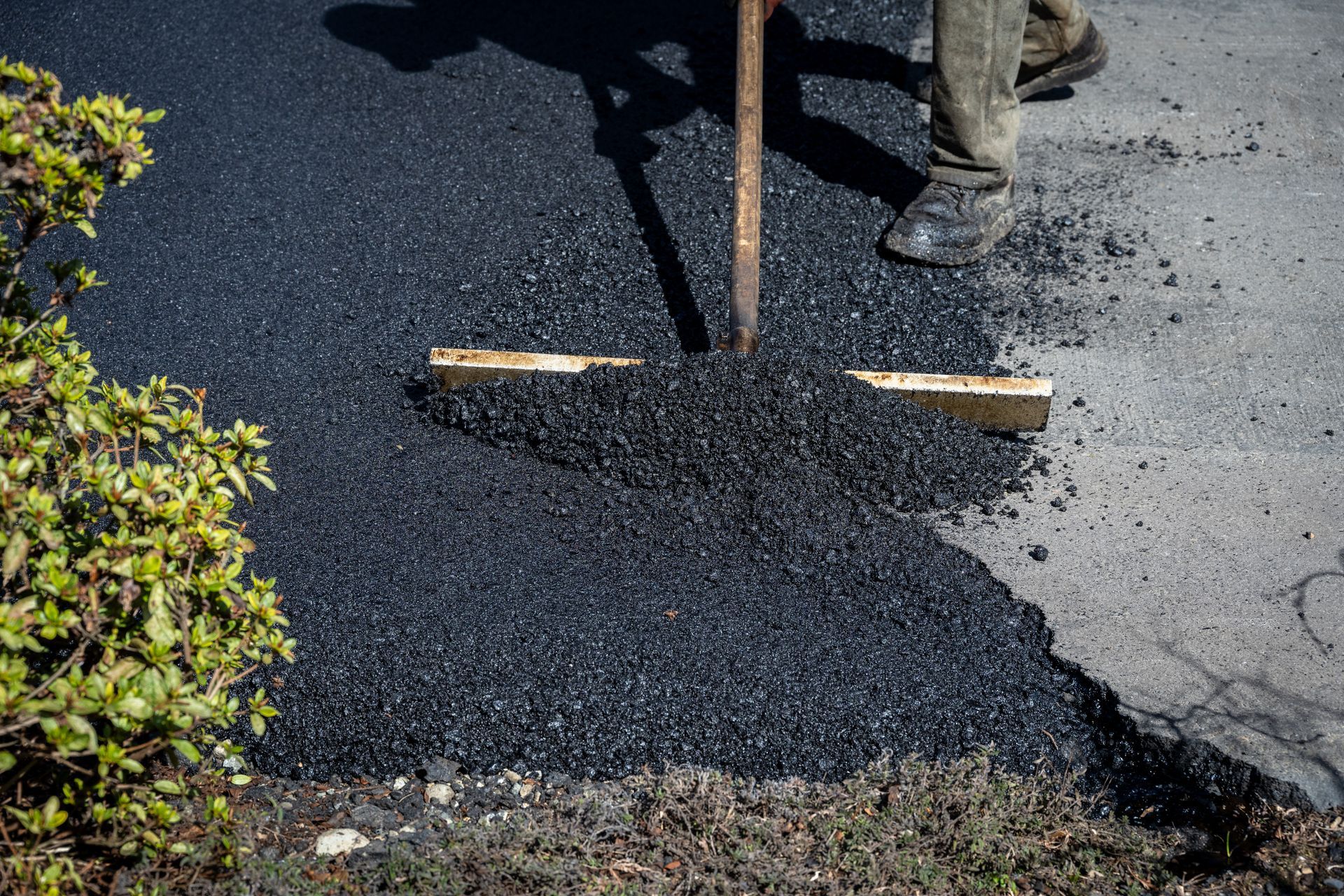 Worker smoothing fresh black asphalt with a rake beside a road curb Worker smoothing fresh black asphalt with a rake beside a road curb