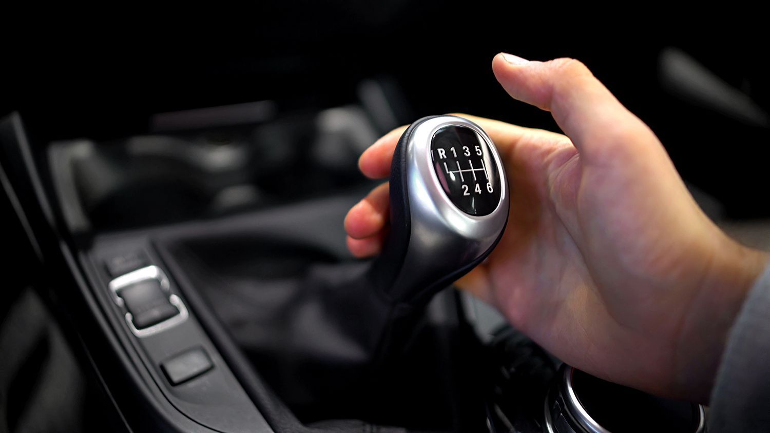 Hand shifting a manual transmission gear stick inside a car.