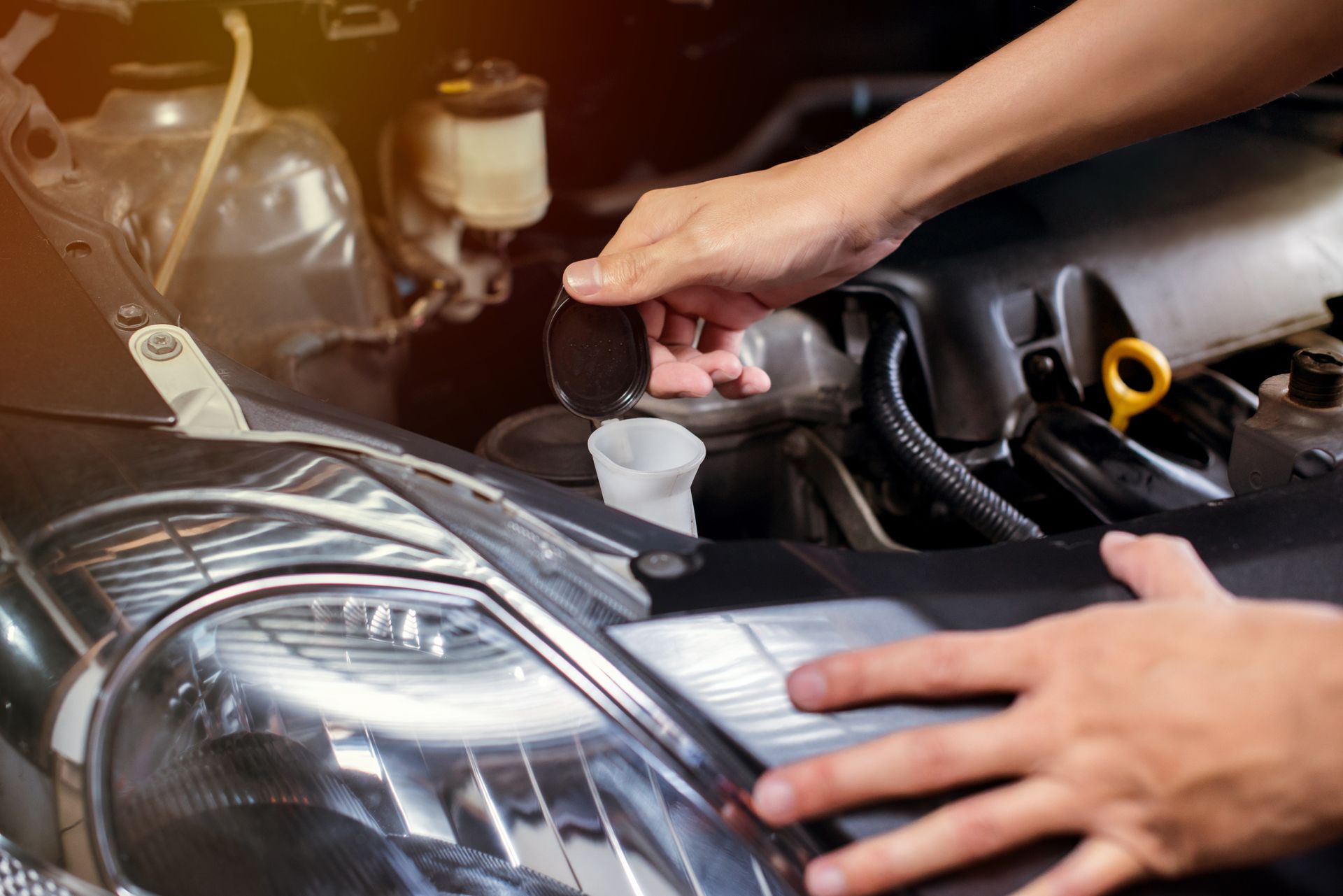 Hands opening a car's windshield washer fluid reservoir cap in the engine bay.