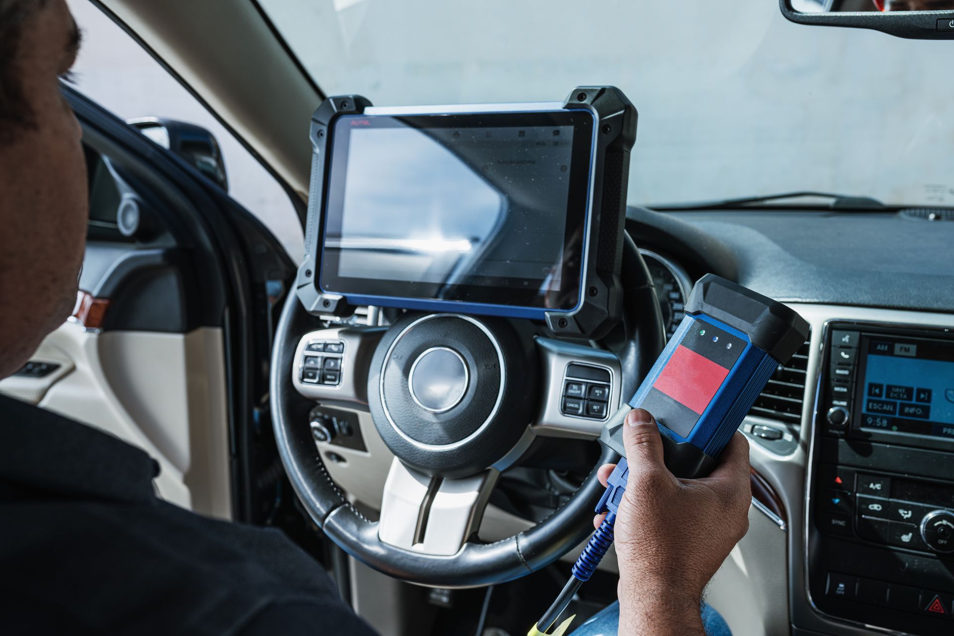 Mechanic using diagnostic tool in a car; tablet mounted on steering wheel.