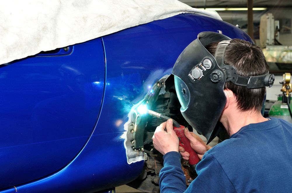 A Man Wearing a Welding Mask is Working on a Blue Car — Marx Forster Tyres & Mechanical In Forster, NSW