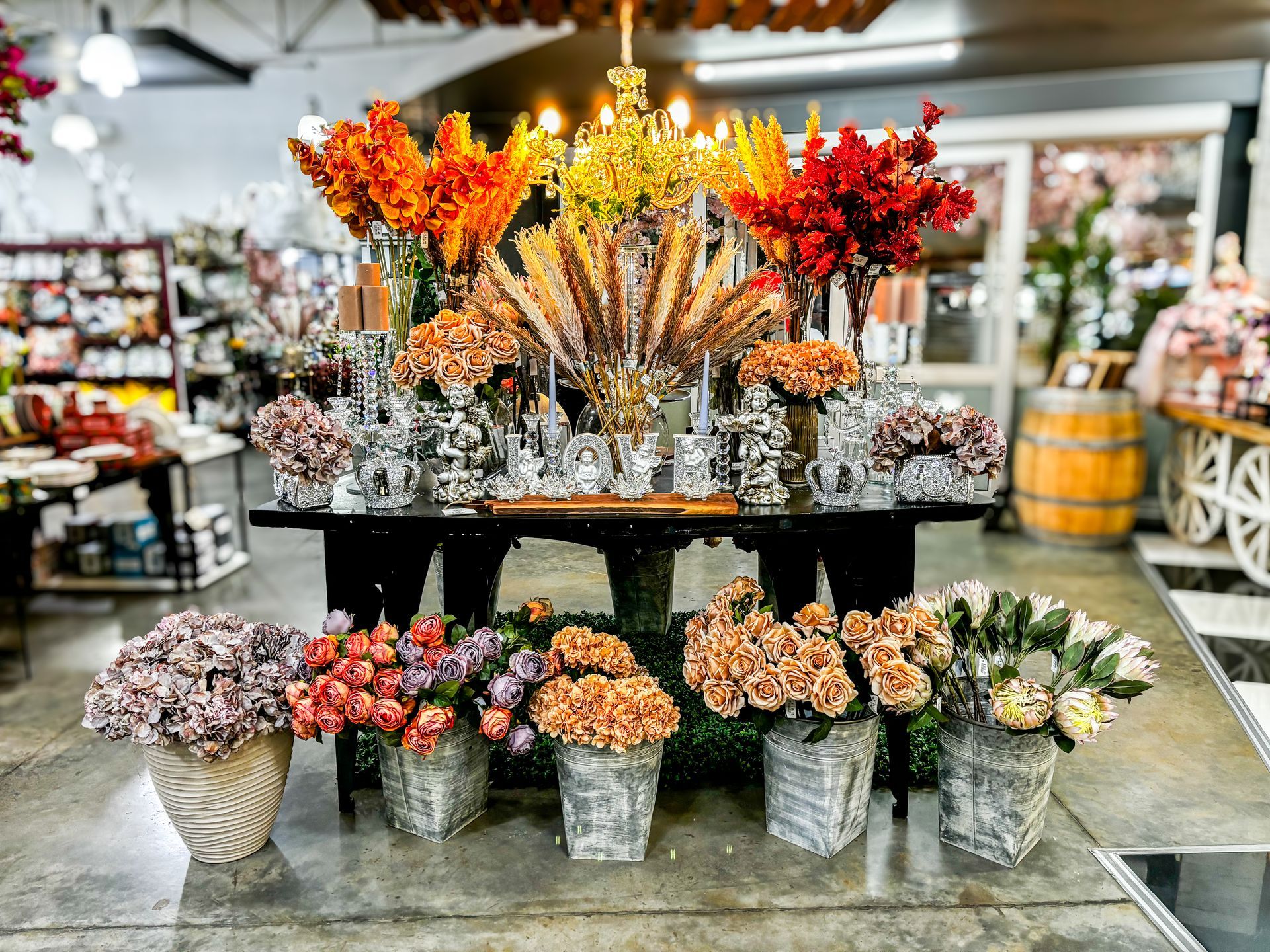 Fresh flowers arranged in a rustic display with vibrant autumn tones, decorative vases, and buckets of seasonal blooms.