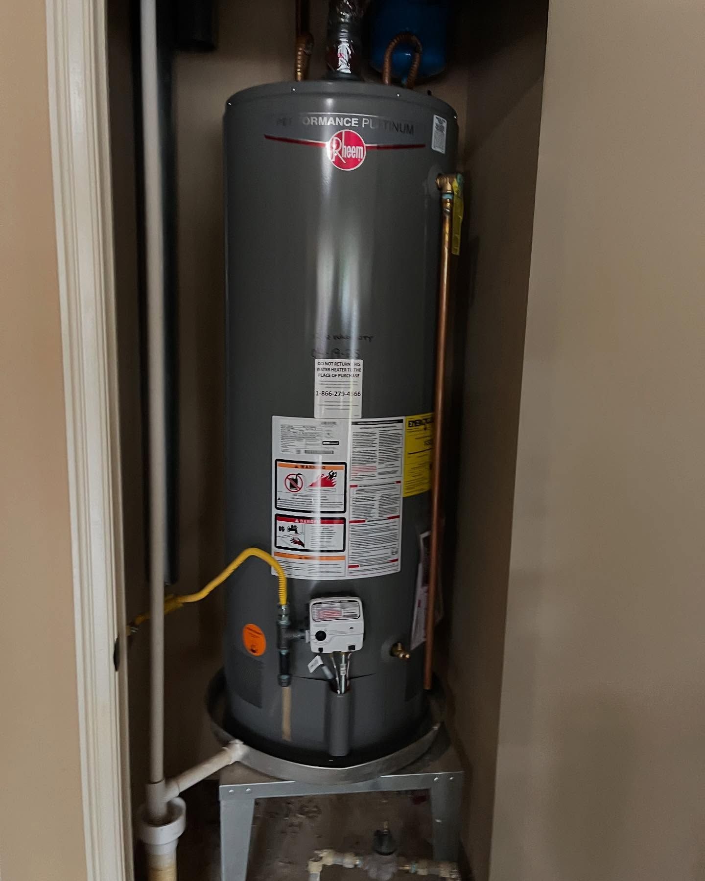 A gray water heater is sitting in a closet next to a door.