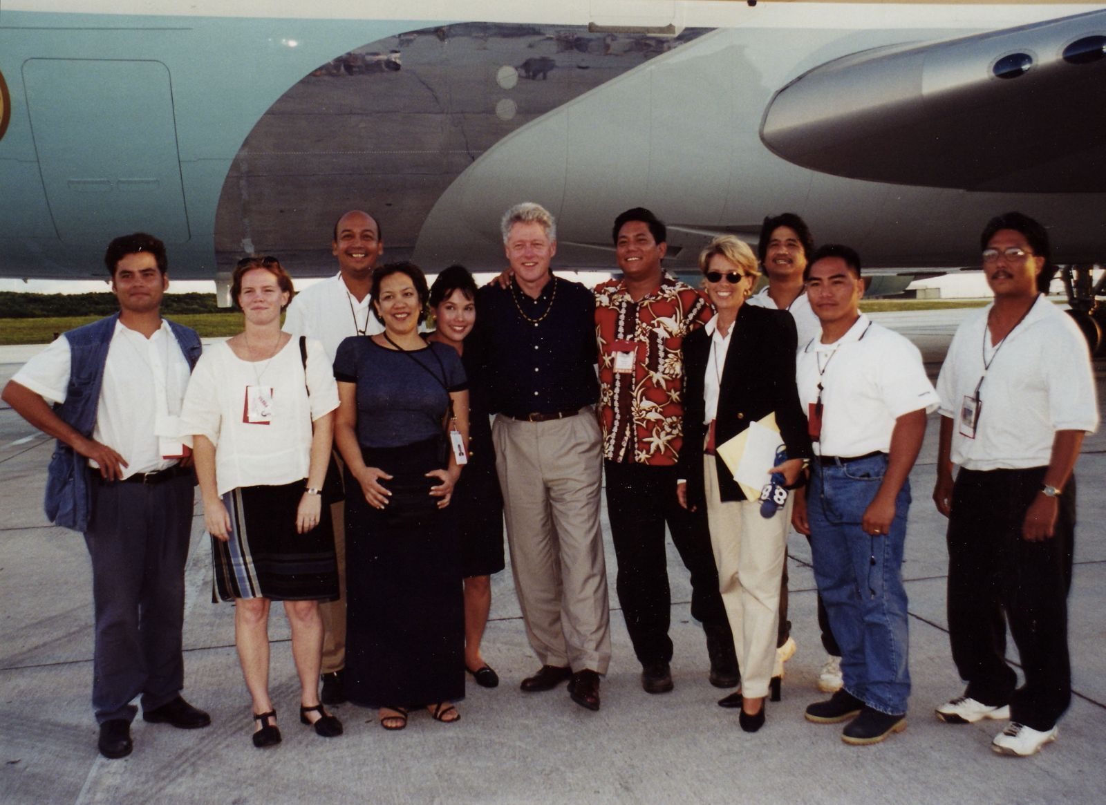 A group of people posing for a picture in front of an airplane with former president Bill Clinton