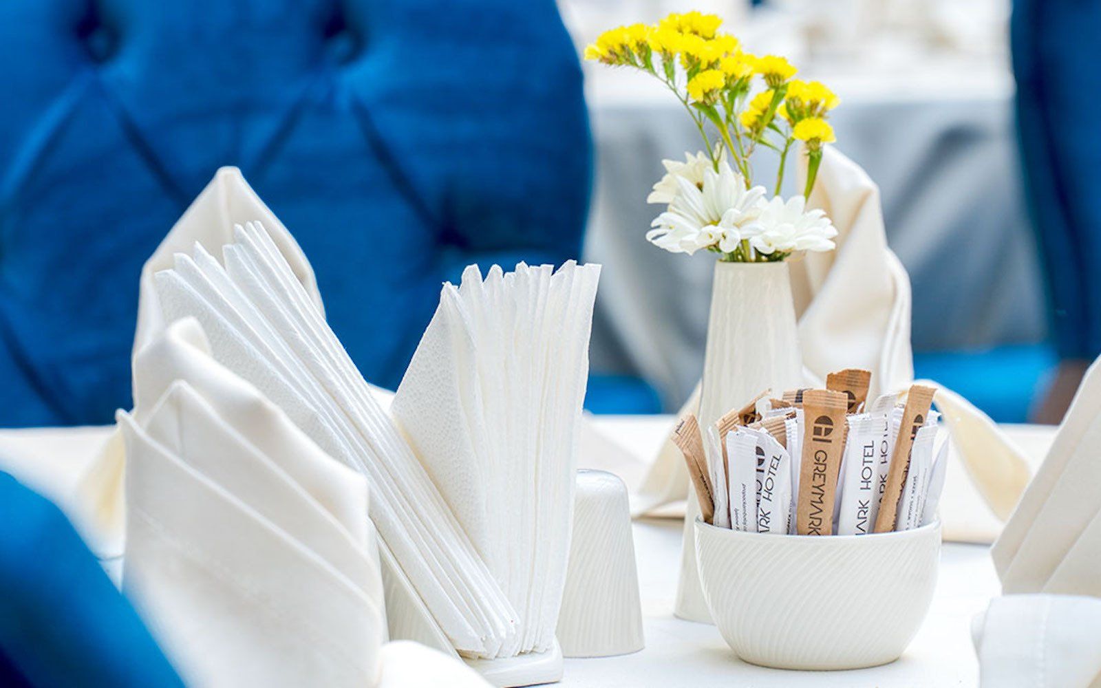 A bowl of sugar sticks sits on a table next to a vase of flowers.