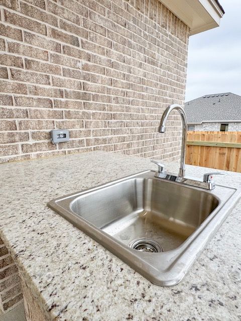 Outdoor kitchen with stainless steel sink, faucet, and speckled granite countertop against a brick wall.
