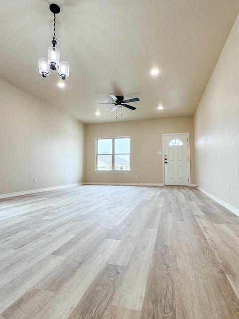Empty, spacious living room with light wood floors, beige walls, and a ceiling fan.