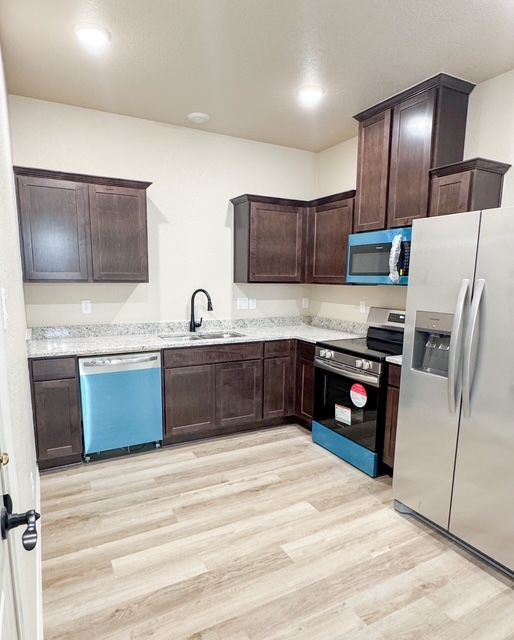 Kitchen with dark cabinets, stainless steel appliances, and light wood-look flooring.