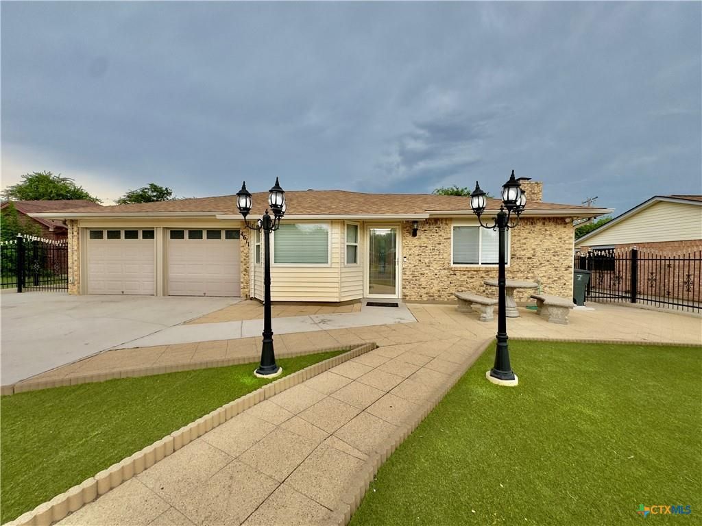 A beige ranch-style house with a pathway flanked by lampposts. Cloudy sky.