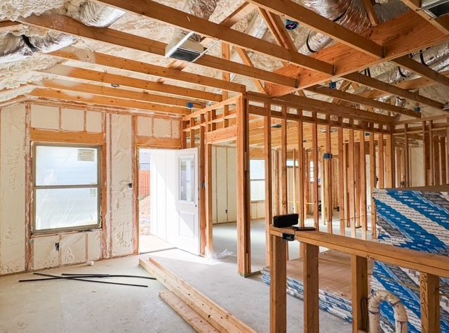 Interior of a house under construction, with wooden framing, insulation, and exposed beams.