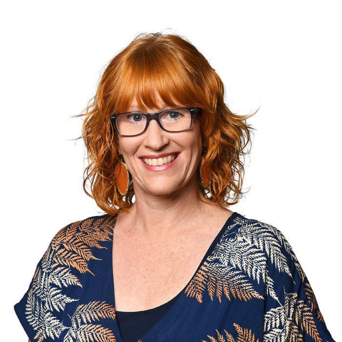 A woman with red hair and glasses is smiling for the camera.