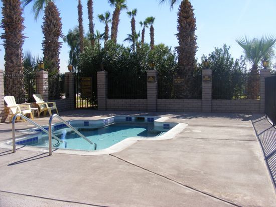 Outdoor hot tub with handrails, surrounded by concrete, fence, and palm trees.