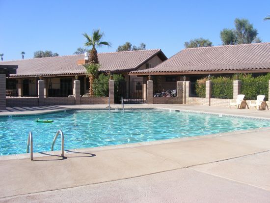 Swimming pool with clear water in front of a building with a tiled roof; two lounge chairs on the right.