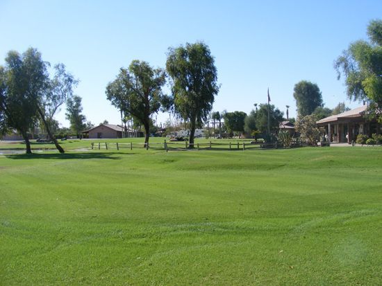 Green grassy field with trees, and buildings under a clear blue sky.