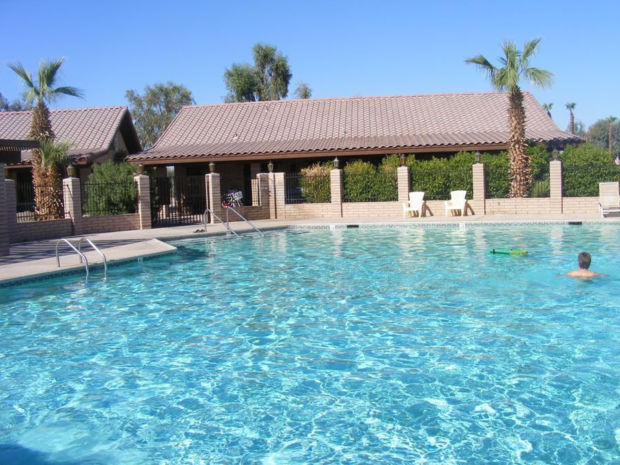 Pool with clear blue water and a tiled roof structure. Palm trees and a swimmer visible. Sunny day.