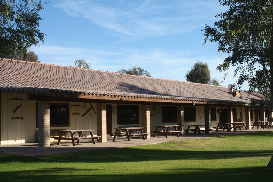 Long, low building with terracotta tile roof and picnic tables on a grassy lawn.