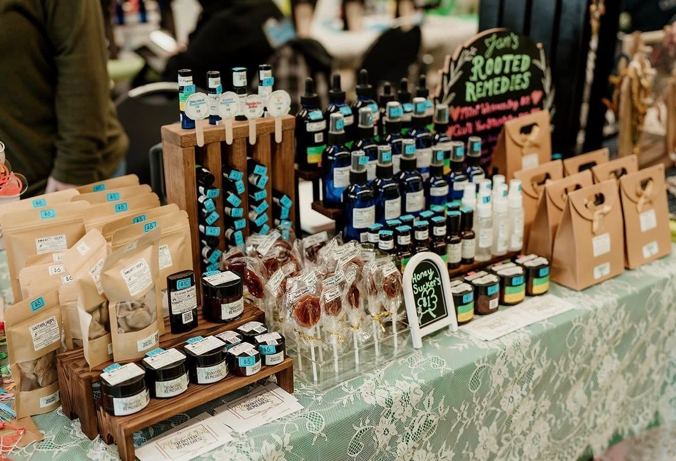 A market stall selling bottled remedies, packaged goods, and lollipops on a green lace-covered table.