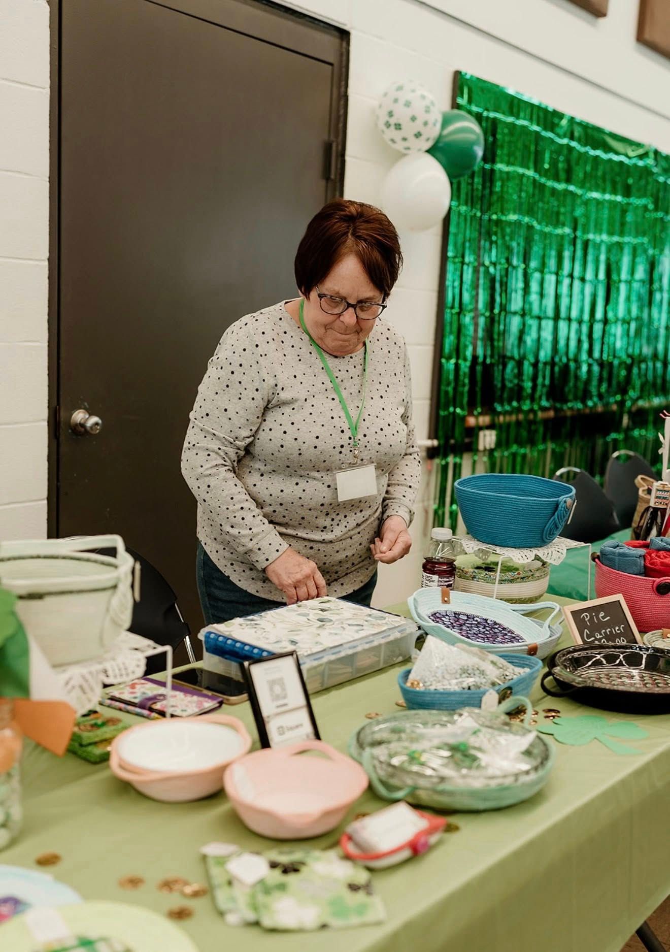A person in a spotted long-sleeve shirt prepares food at a table decorated with green accents, balloons, and bowls.