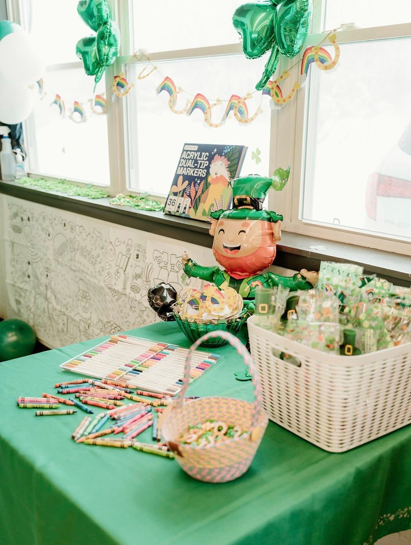 A St. Patrick's Day party table with a green tablecloth, a leprechaun balloon, festive snacks, and a basket of favors.