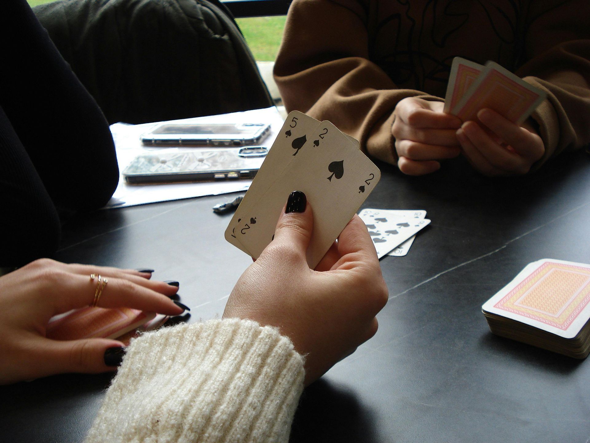 A hand rests on a tarot card next to a spread of teal cards, small bowls of crystals, herbs, and three lit candles.