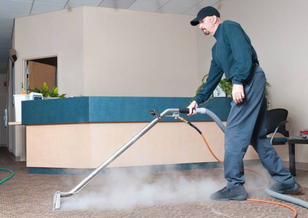 A person in a jumpsuit cleaning a dark carpeted room with a flat mop.
