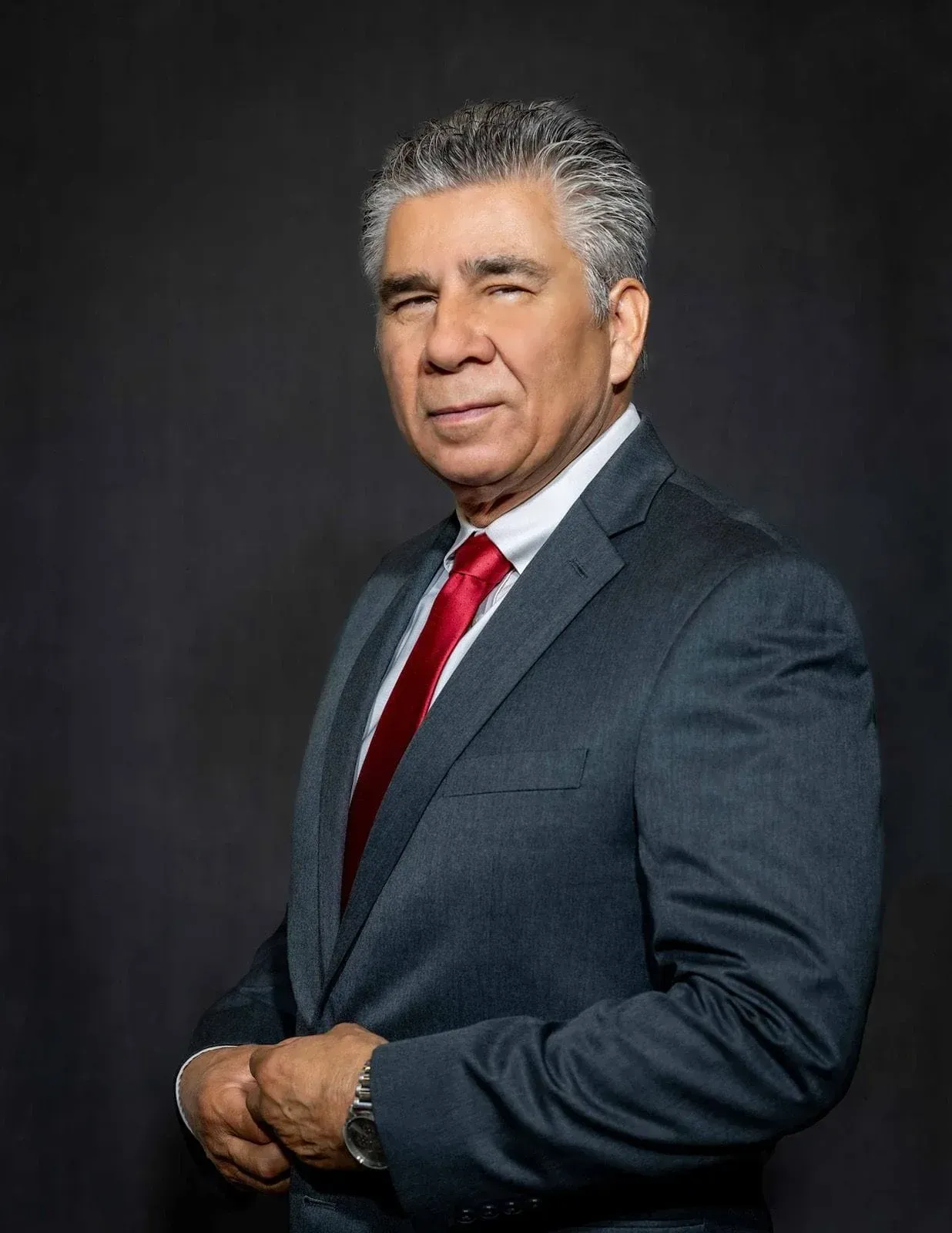 Portrait of a man in a dark suit and red tie against a dark background.