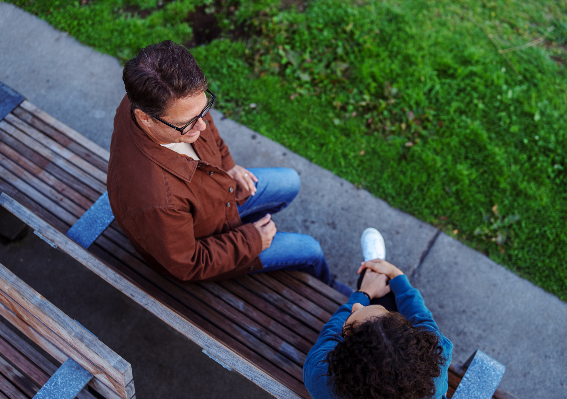 A man and a woman are sitting on a bench talking to each other.