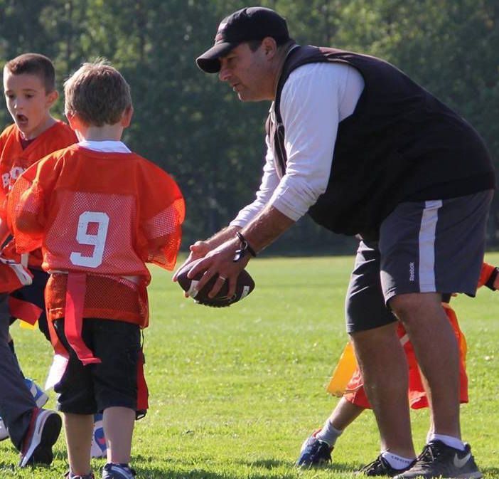 A man holds a football in front of a boy with the number 9 on his jersey