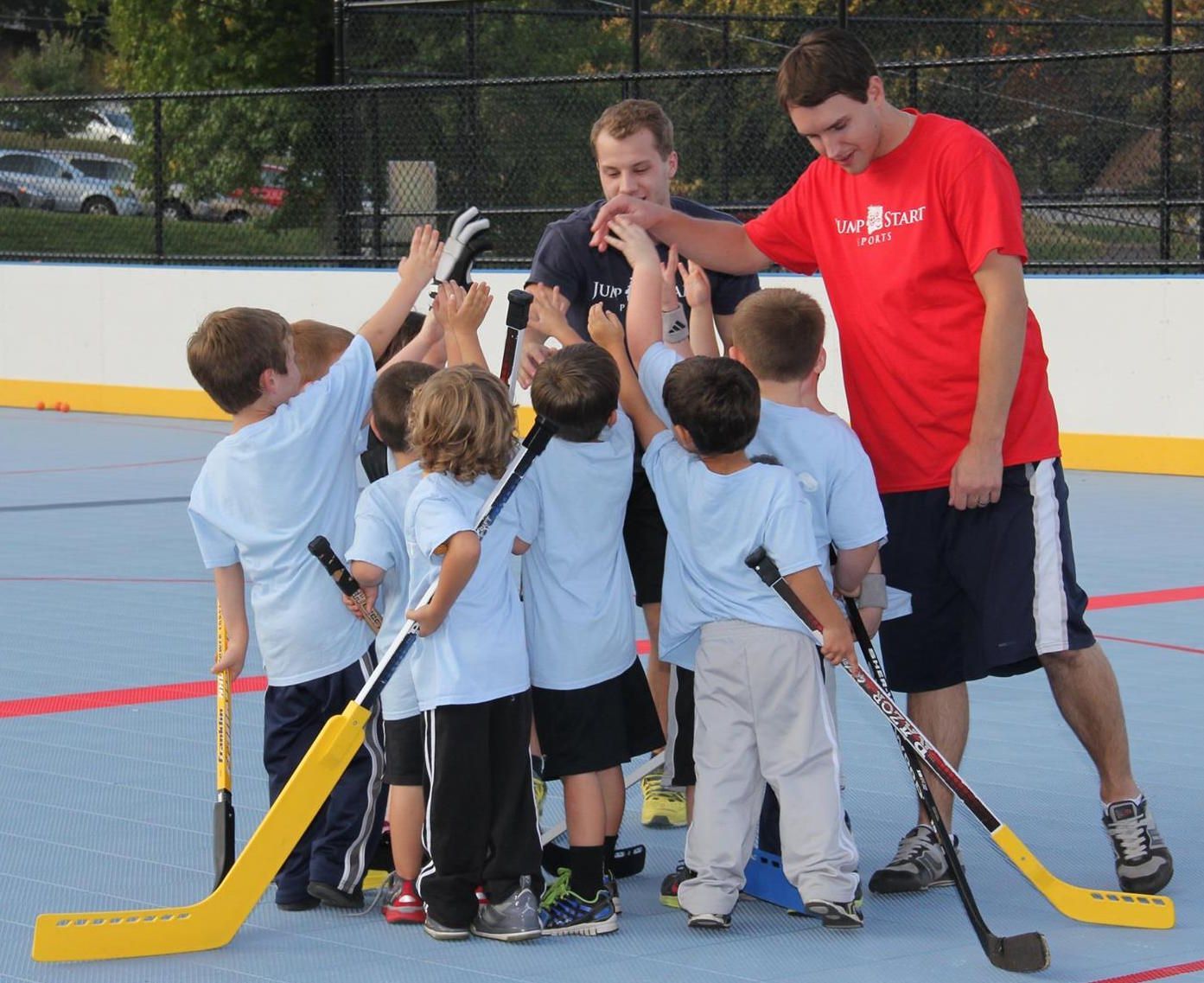 A man in a red shirt is giving a high five to a group of young hockey players