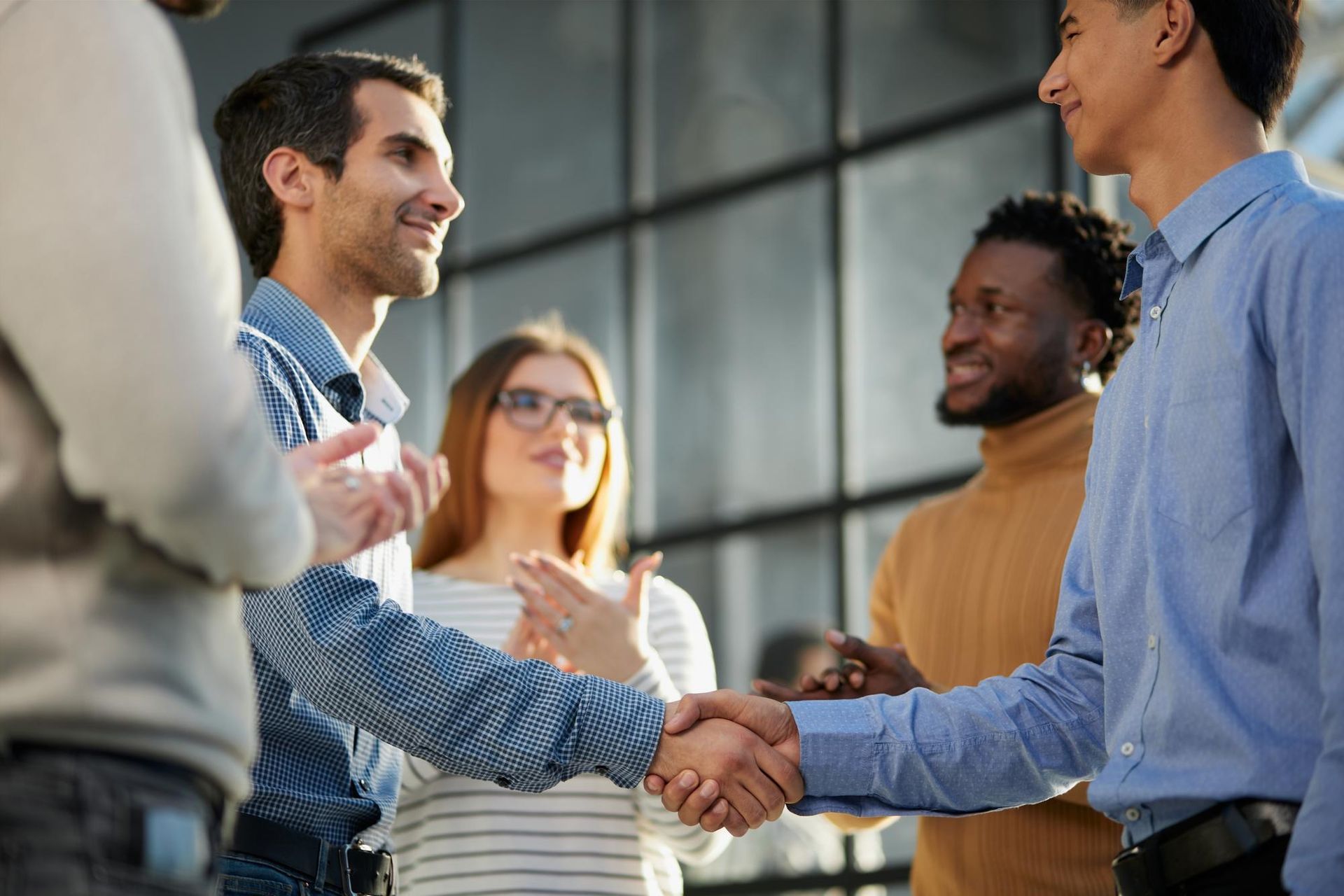 Four colleagues shaking hands in a modern office lobby, smiling during a business meeting