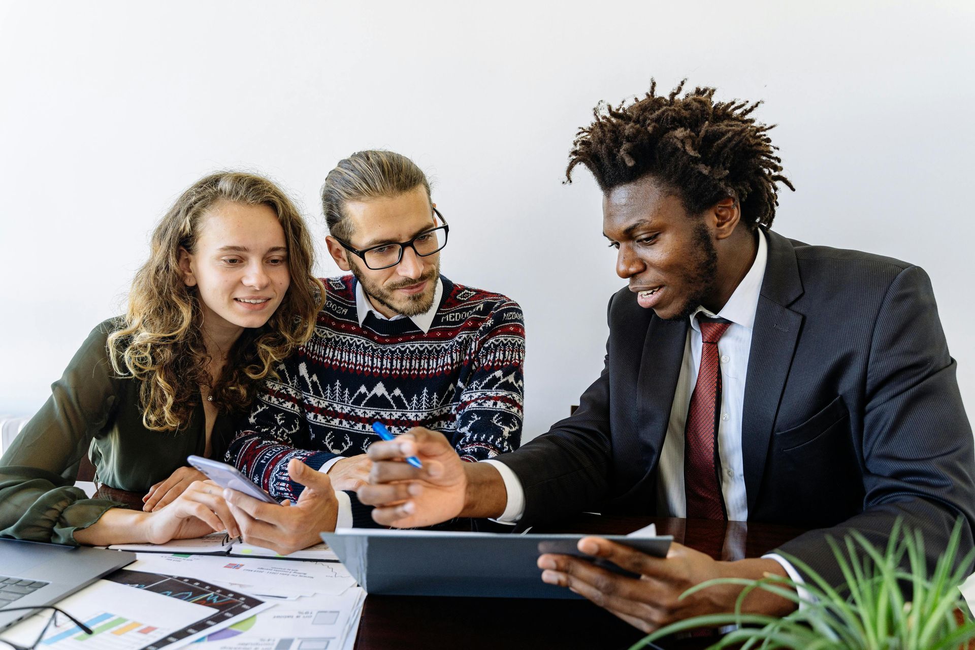 Three coworkers collaborating at a table, discussing notes and using a tablet in an office setting.
